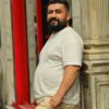 God stil Portrait of a bearded man in casual attire leaning against a column outdoors.